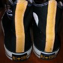 Brad Deniston Collection of Chucks  Rear view of black and gold 2-tone high tops with black and white reversible shoelaces.
