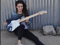 Meg Myers  Meg seated with her guitar wearing optical white low cut chucks.