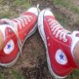 Red High Top Chucks  Seated outdoors on the ground wearing a loosely laced pair of red high top chucks