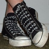 Worn Black High Top Chucks  Crossed leg front view of worn black high tops with checkered straight lacing.